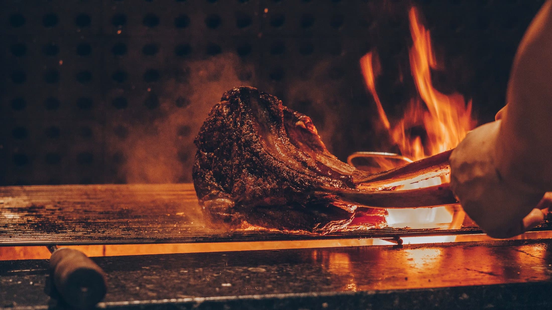 A thick steak searing over open flames on a grill